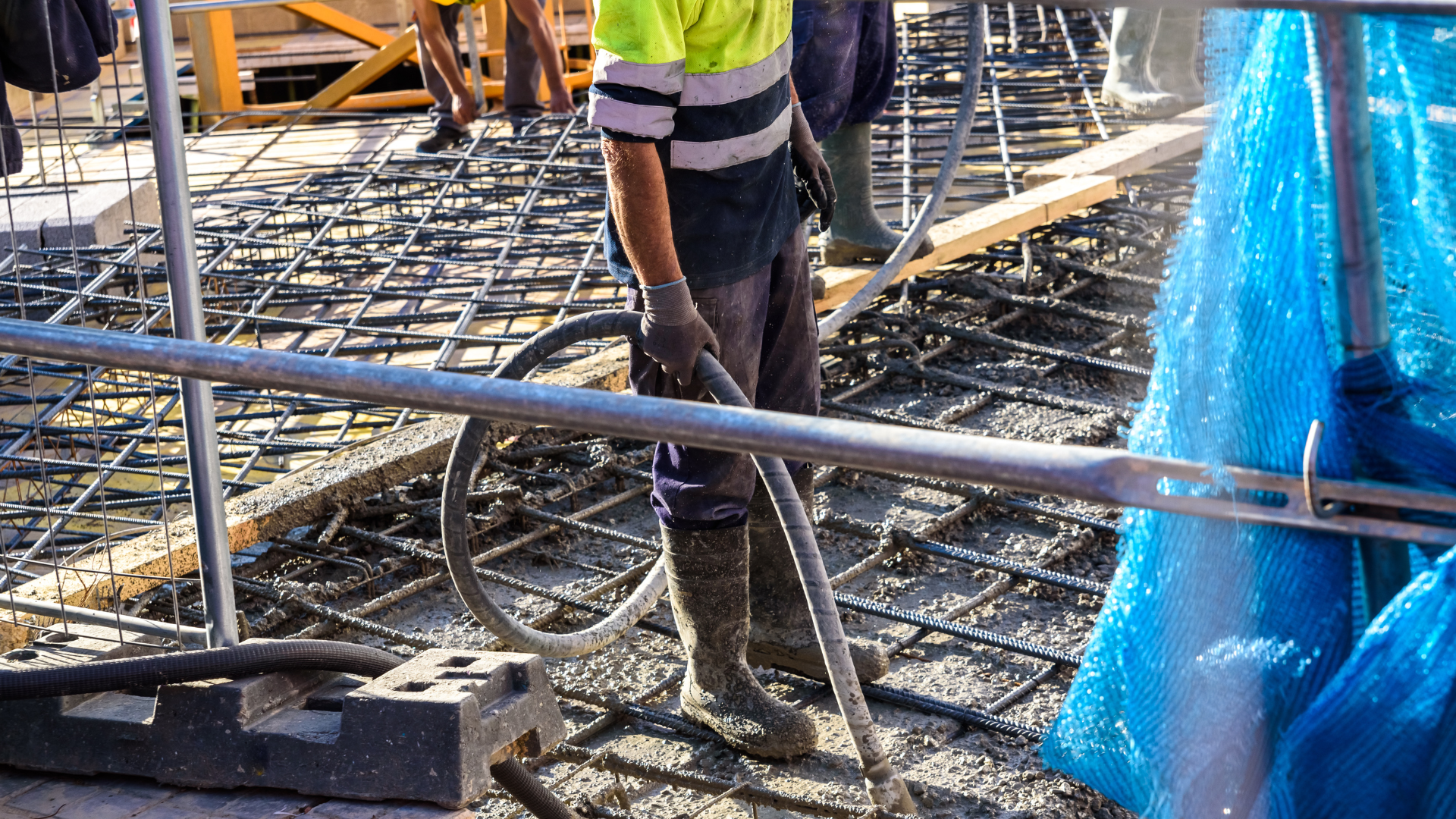 Työntekijät rakennustyömaalla teräsraudoituksen päällä tekemässä betonivalua. Työturvallisuuskoulutus rakentamisen aloille.